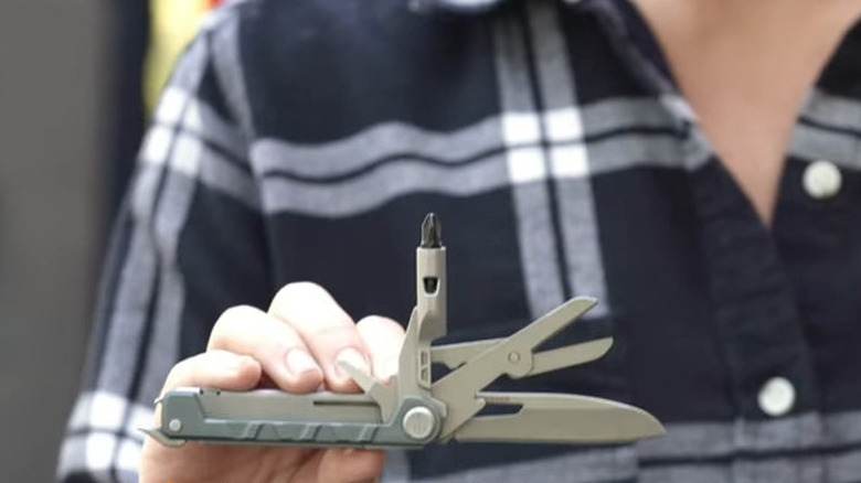 Person holding a green multitool with tools extended
