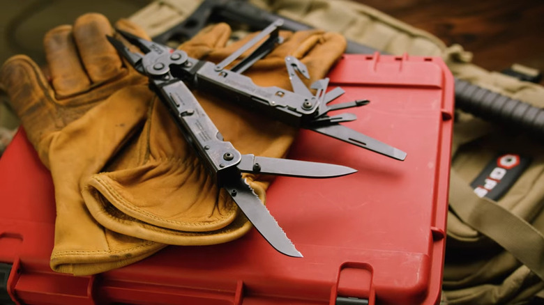 A black multitool with tools opened up on a pair of work gloves, on top of a toolbox