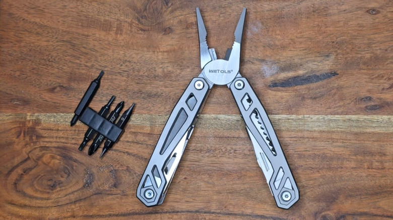 A silver multitool with open pliers and a set of double-sided bits on a wooden table