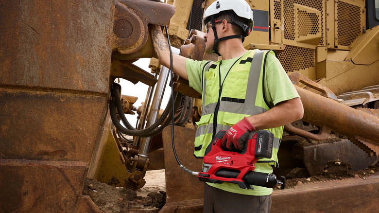 Worker using a Milwaukee M18 Fuel grease gun on construction equipment