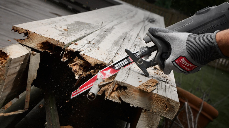 A person using a sawzall to cut a piece of wood with metal