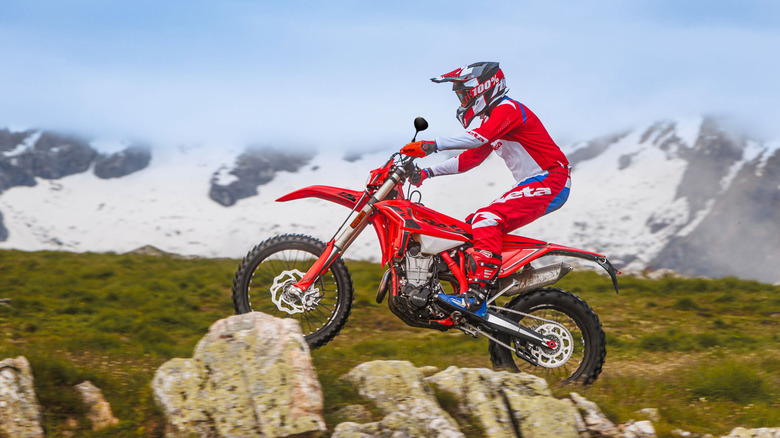 A rider in full gear and helmet taking a red Beta 500RS off-road over some huge rocks with ease.