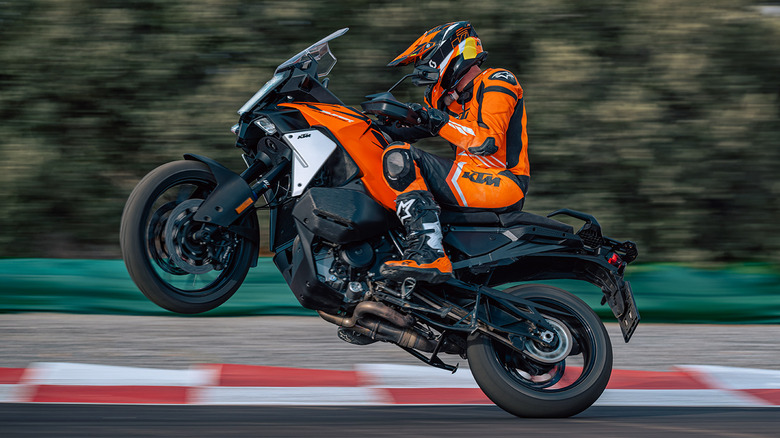 A fully-kitted out motorcyclist on a 2026 KTM 1390 Super Adventure S EVO motorbike on a track, front wheel in the air.