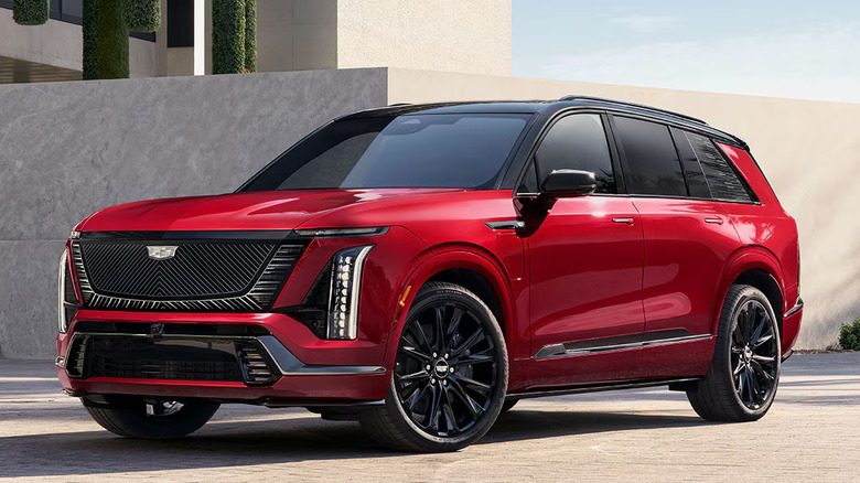 A  red 2026 Cadillac Vistiq parked next to modern stone buildings outside, left three-quarter view shown.