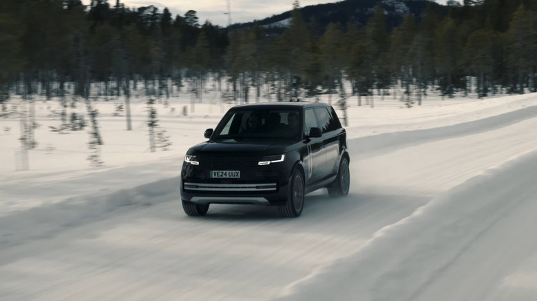 A blue 2026 Range Rover Electric EV moving at speed down a snow-covered road, with trees and hills in the back.