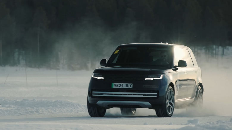 A dark blue 2026 Range Rover Electric kicking up snow on a road in the winter with silver accents.