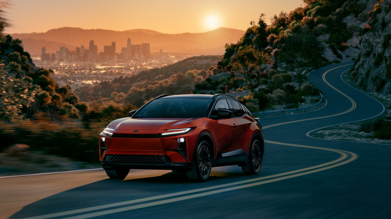 An orange 2026 Toyota C-HR electric variant moving down a curving mountain road as the sun sets.