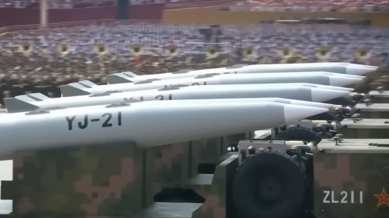Several YJ-21 missiles lined up in a row, on top of trucks, as part of a parade.