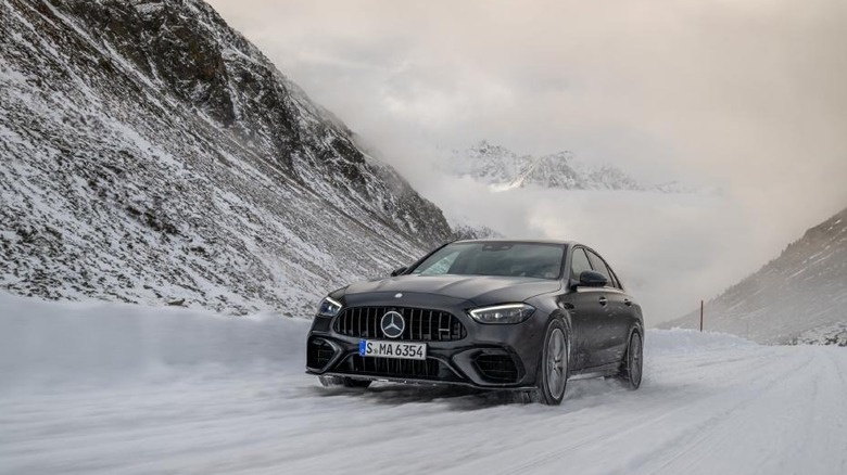 A black 2025 Mercedes-AMG C-Class sedan driving on a snow-covered mountain road.