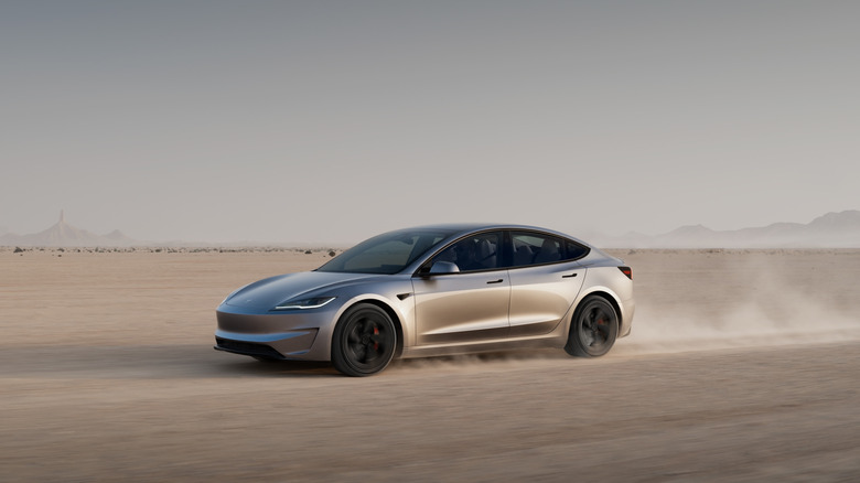 A silver 2025 Tesla Model 3 kicking up dust while driving across a desert landscape.