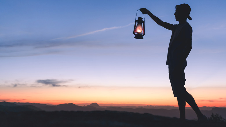 Silhouette of a man holding a lit kerosene lamp to light his way in the dark.