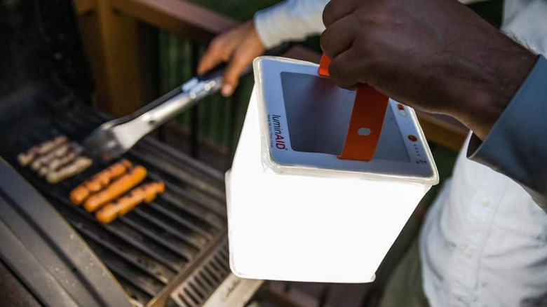 A man holding the LuminAID PackLite Titan while cooking up some barbecue.