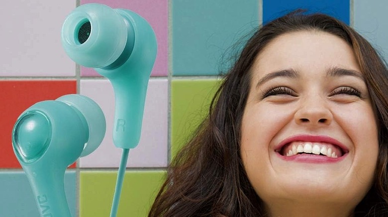 A woman smiling next to a pair of JVC Gumy earbuds.