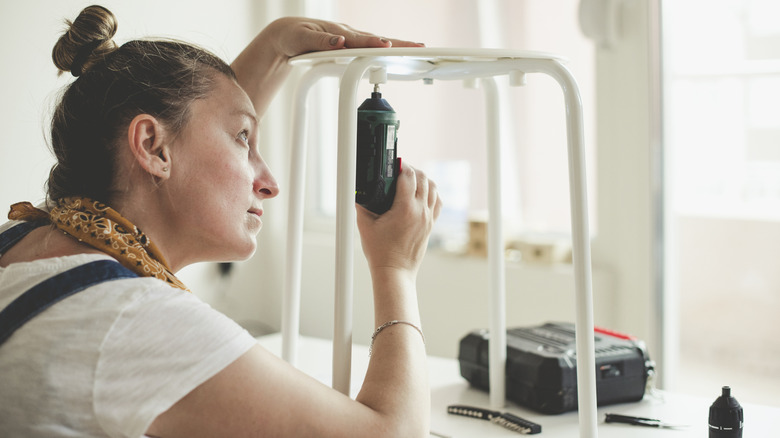 person using electric screwdriver on stool