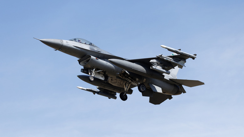 An under-body view of an F-16 flying oerhead against a clear blue afternoon sky