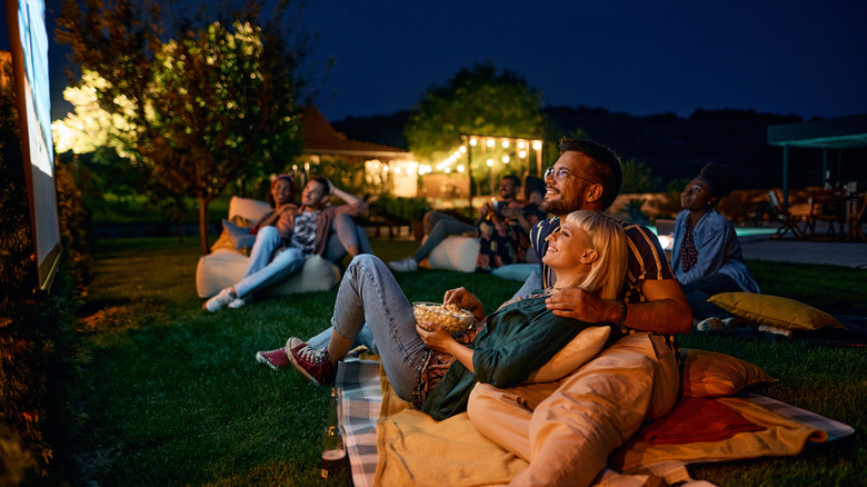 A group of friends watching a movie in the evening in the backyard.