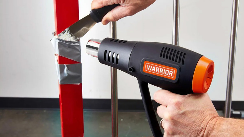 A man using a heat gun to melt duct tape on a red metal post