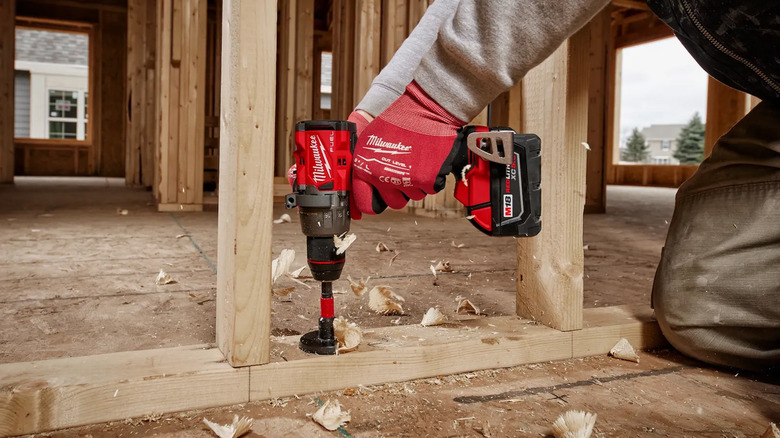 A construction worker using a Milwaukee drill to cut a hole in wood