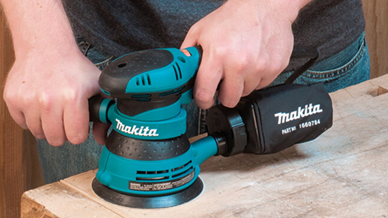 A man using a Makita random orbital sander on a piece of wood
