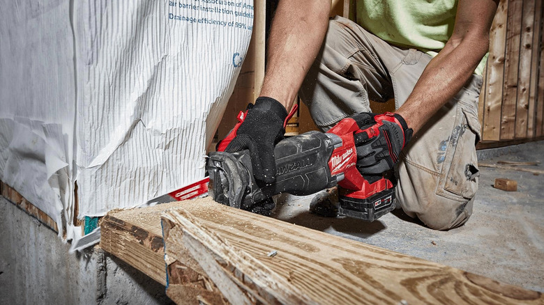 A worker cutting a piece of wood with a Milwaukee Sawzall