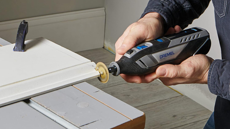 A man cutting a baseboard with a Dremel 8250