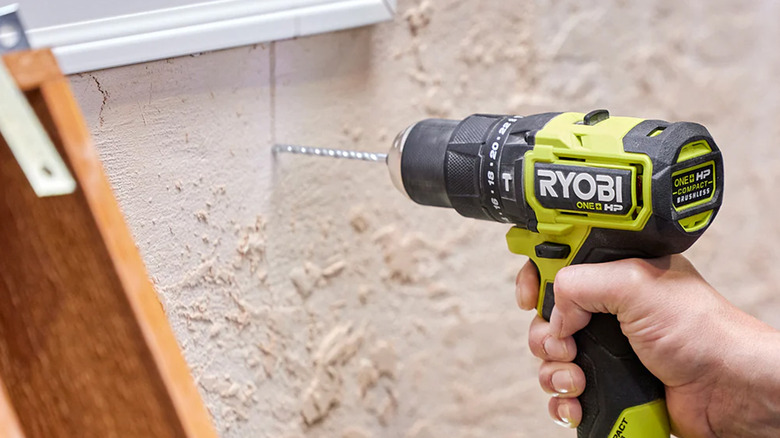 A person drilling a hole in an exterior wall with a Ryobi drill