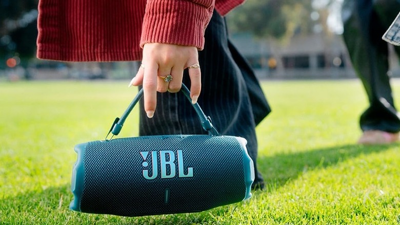 Carrying a JBL speaker with a handle on a grassy field.