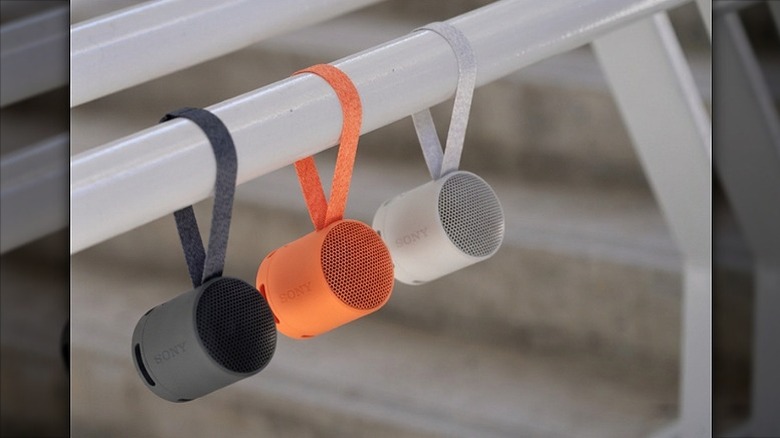 Three Sony speakers  -- black, orange, and white -- hanging from a white rod.