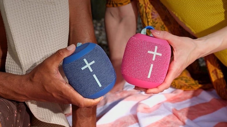 A man and woman holding blue and pink WonderBoom 4 speakers