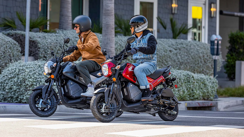 Two riders, a man and a woman, wearing helmets while riding a black and a red Honda Navi