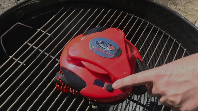Grillbot grill-cleaning robot on a grill, being activated by hand.