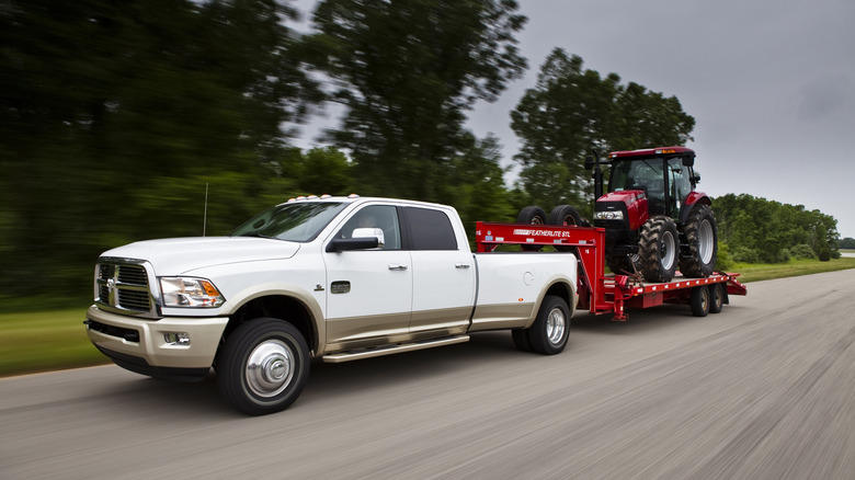 A 2013 RAM 3500 longhorn towing a tractor down an evening road