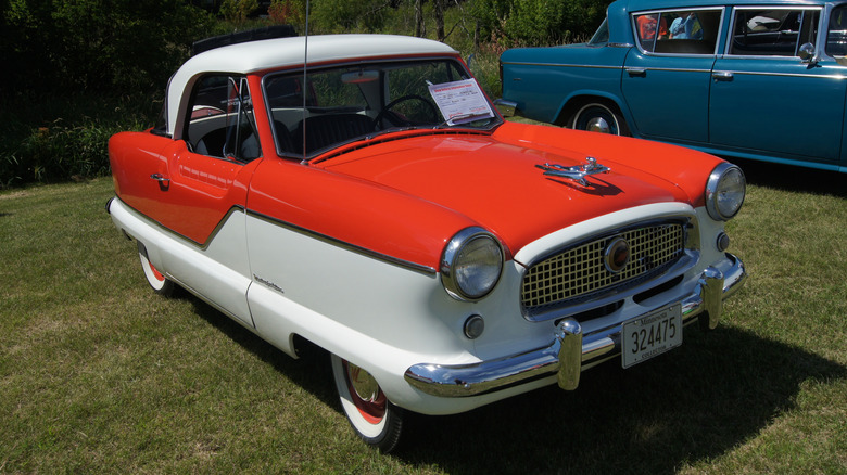 Red and white 1958 Nash Metropolitan on display in an outdoor car show
