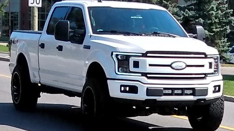 A white Ford F-150 with whited out badging on a city road.