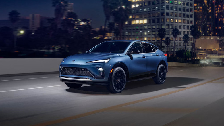 A deep blue 2026 Buick Envista SUV moving at speed down a paved road, with buildings visible but blurry in the back.