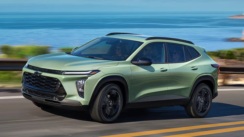A green 2026 Chevrolet Trax being driven at speed down a road with a body of water in the backround.