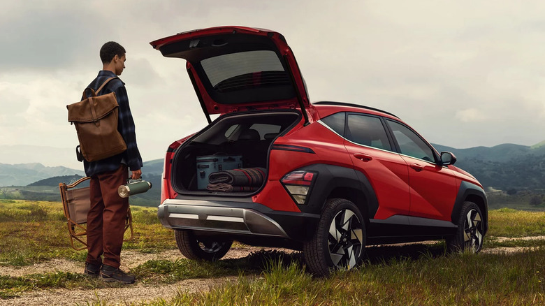 An orange 2026 Hyundai Kona standing in a barren field with its rear liftgate open and a man standing next to it.