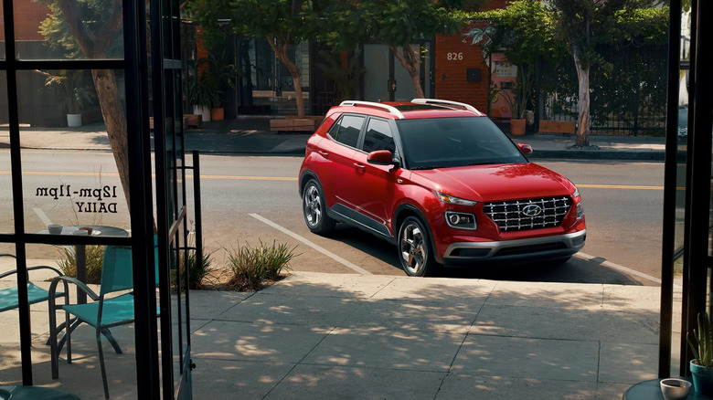 A red 2026 Hyundai Venue finished in red metallic, standing outside a café in a parking bay.