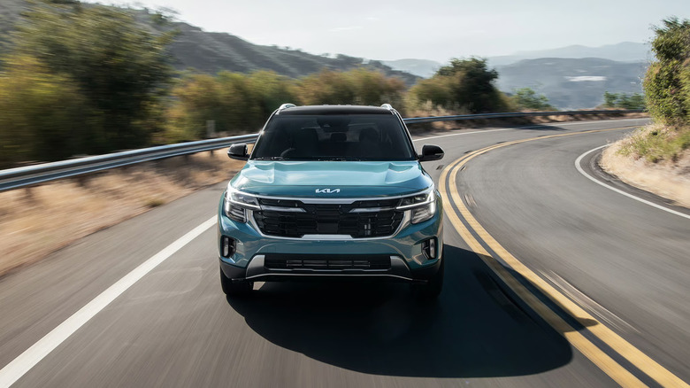 A light blue 2026 Kia Seltos taking a turn at speed down a mountain road, front-on view visible.