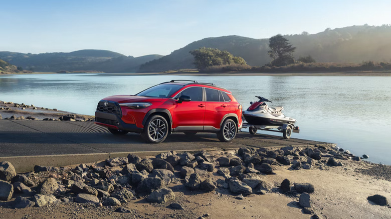 A red Toyota Corolla Cross SUV towing a jetski from an asphalt slip on the shores of a lake.