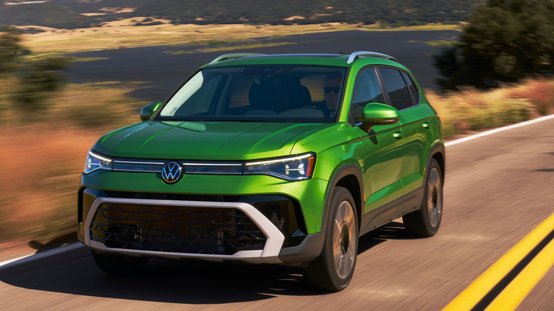 A dark green 2026 Volkswagen Taos being driven at speed down a two-lane road.
