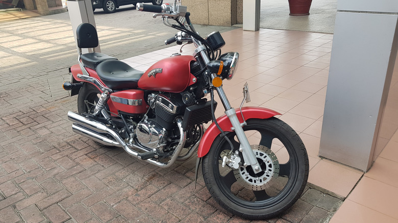 A red and black 2020 Harley-Davidson Low Rider ST parked next to to a pillar on a brick surface.