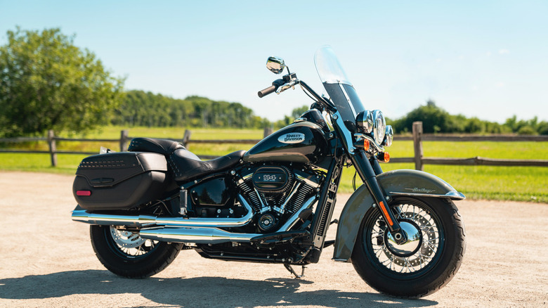 A black Harley-Davidson Haritage Classic 114 from the 2021 model year parked on a road with a field in the background.