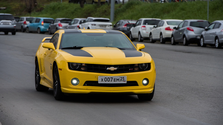 A yellow-and-black Chevrolet Camaro driving down a road