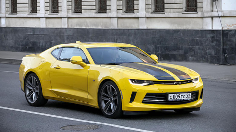 A yellow Chevrolet Camaro with black lines on its bonnet cruising.
