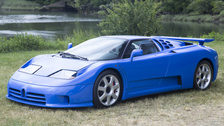 Blue 1995 Bugatti EB110SS supercar seen from left front parked on grass by a pond
