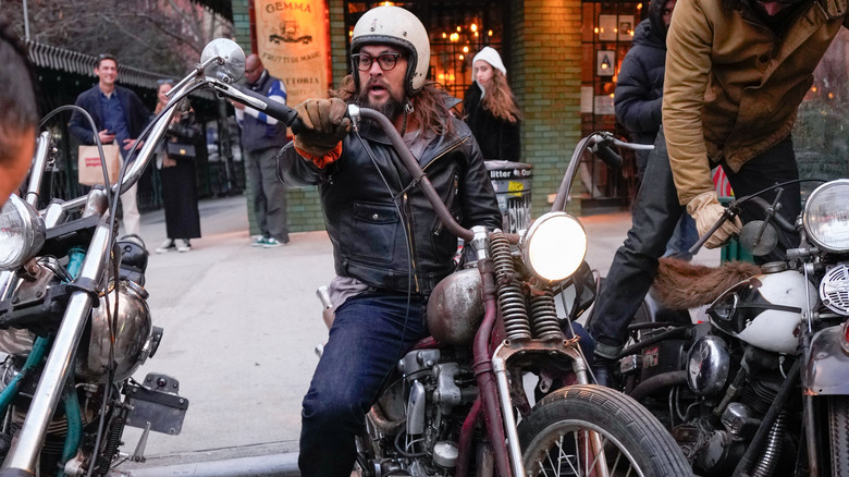 Jason Momoa sitting on a Harley playing a guitar