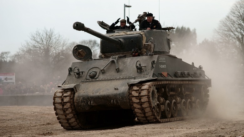 Several men operating an M4 Sherman Tank on a dirt road.