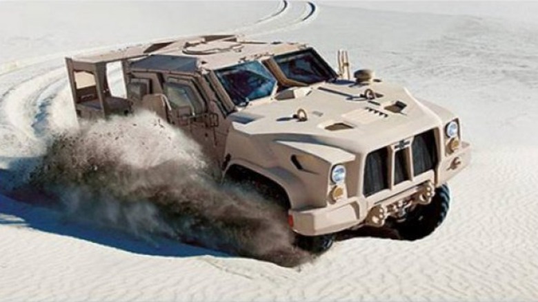 An Oshkosh L-ATV driving in the desert while kicking up sand.