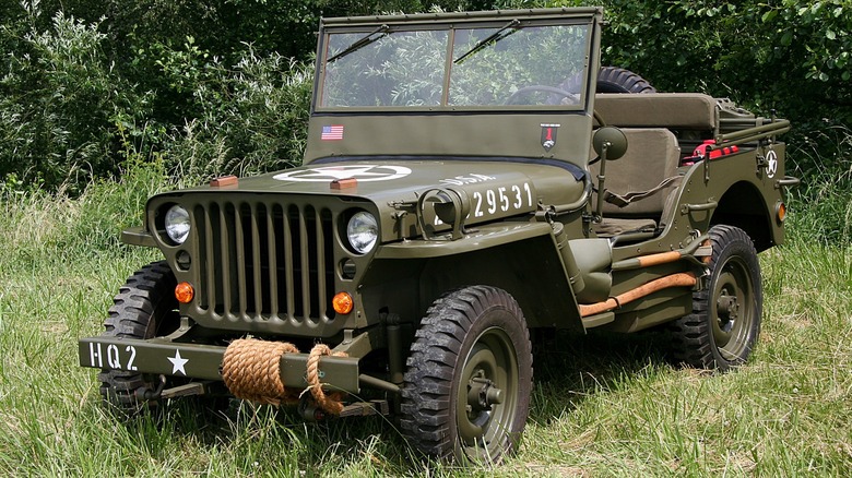 A Willys MB army Jeep parked in tall grass by a treeline.